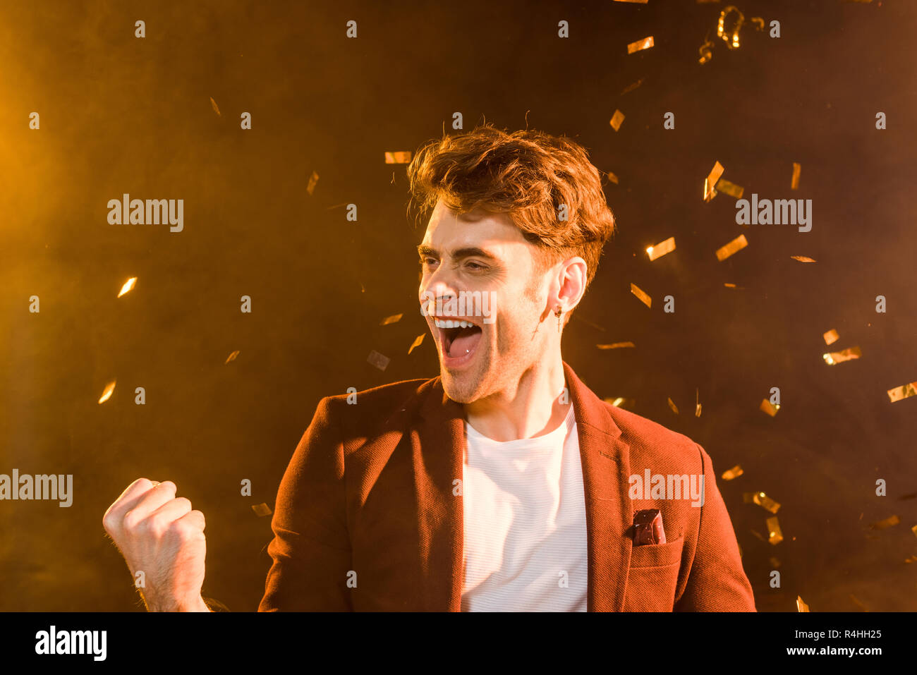 celebrating young man under falling confetti on black Stock Photo
