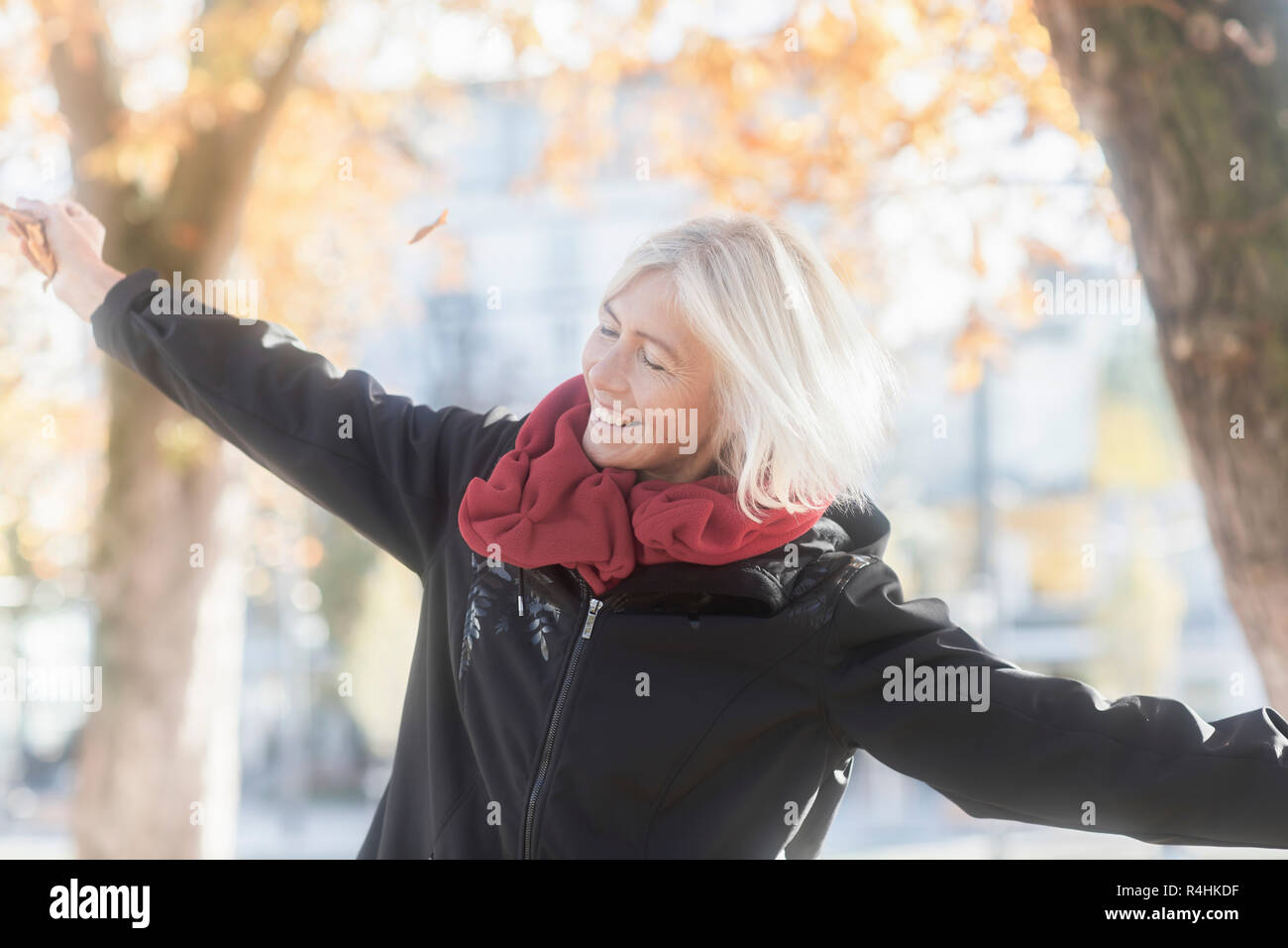 Portrait of a smiling woman standing in the park with her arms ...
