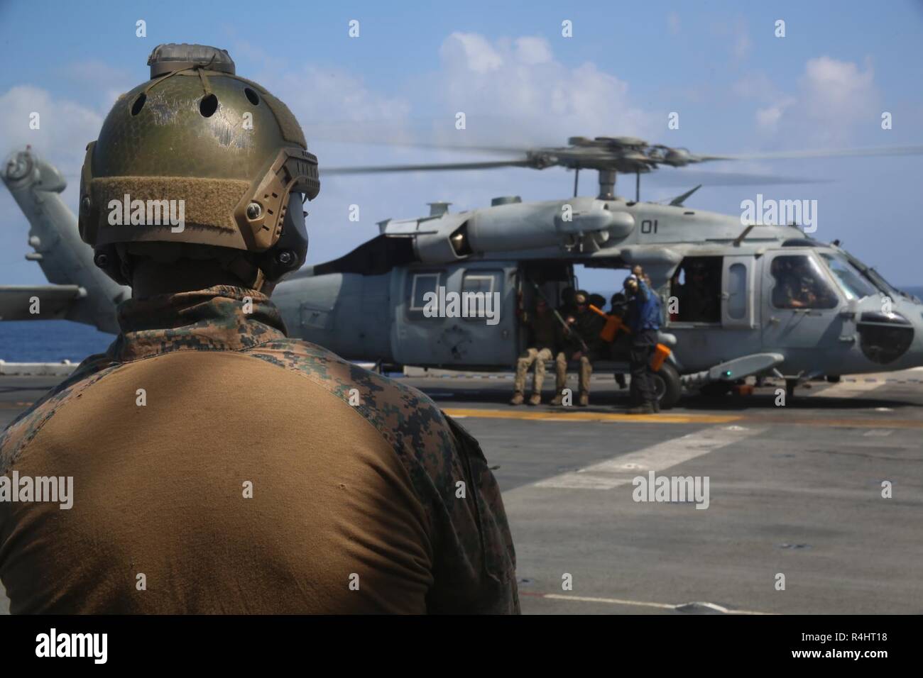 xxxGunnery Sgt. Jesus Cisneros Jr., the platoon sergeant for the 31st Marine Expeditionary Unit’s Amphibious Reconnaissance Platoon, watches an MH-60S Seahawk prepare for takeoff during Visit, Board, Search and Seizure training aboard the amphibious assault ship USS Wasp (LHD 1), while underway in the South China Sea, Sept. 29, 2018. Cisneros, a native of Lake Station, Indiana, graduated River Forest High School, May 1997; he enlisted in January 2004. During the training, ARP Marines refined their fast rope capabilities while Marines with the Security Platoon held aerial security to help simul Stock Photo