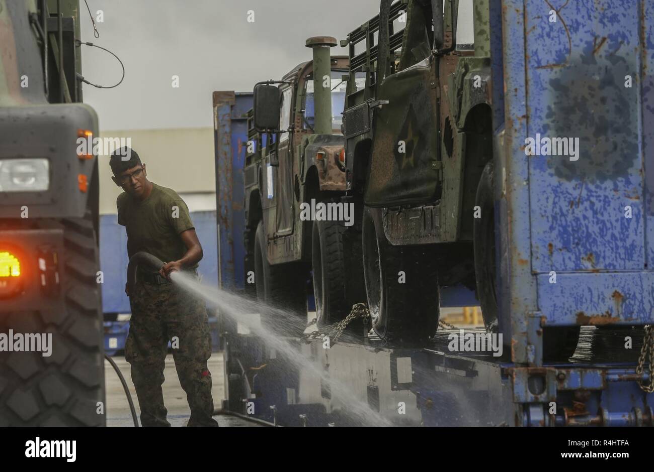 A U.S. Marine with II Marine Expeditionary Force sprays off a trailer before storing them on USNS Wright (T-AVB 3) before embarkation to Norway at the Port of Morehead City in Beaufort, N.C., Sept. 28, 2018. These vehicles will be used as part of II MEFs participation in the NATO-led Exercise Trident Juncture 18 in Norway, Sweden, Finland, and Iceland. Trident Juncture 18 enhances the U.S. and NATO Allies’ abilities to work together collectively to conduct military operations under challenging conditions. Trident Juncture will include more than 14,000 U.S. service members and 31 Allied and par Stock Photo