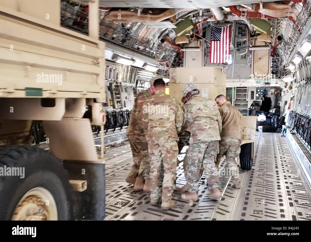 Soldiers from Headquarters and Headquarters Company, 89th Military Police Brigade, Task Force Griffin, load a 30K generator on a C-17 aircraft as the American Flag flies in the background, October 29, 2018. Soldiers from Task Force Griffin are deploying to the Southwest Border Region to support and enable Department of Homeland Security and other law enforcement agencies as they conduct coordinated efforts to secure our southwest border. Stock Photo