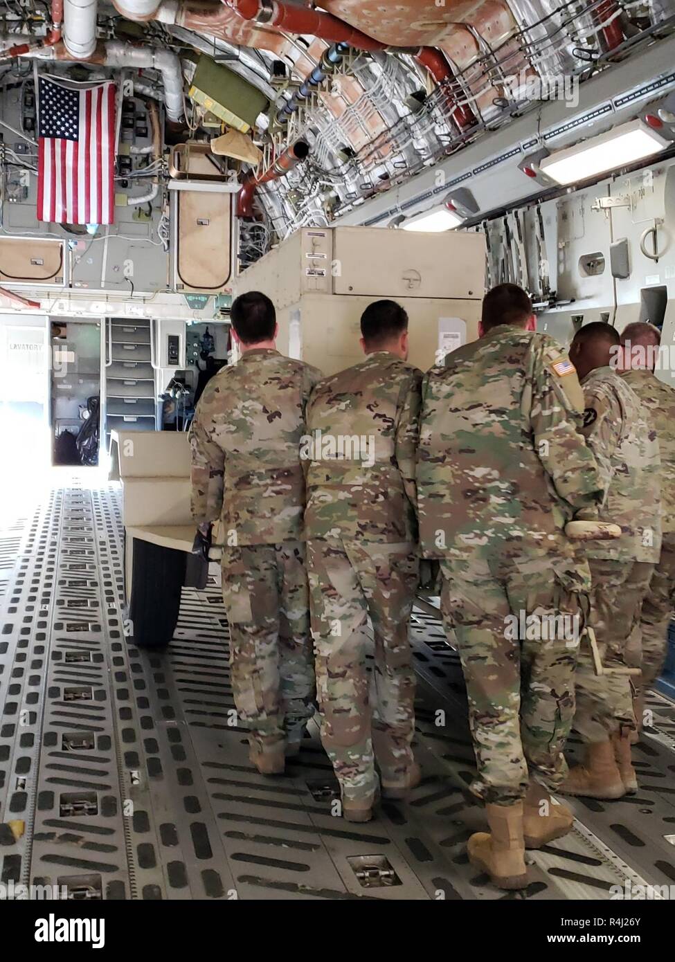 Soldiers from Headquarters and Headquarters Company, 89th Military Police Brigade, Task Force Griffin, load a 30K generator on a C-17 aircraft as the American Flag flies in the background, October 29, 2018. Soldiers from Task Force Griffin are deploying to the Southwest Border Region to support and enable Department of Homeland Security and other law enforcement agencies as they conduct coordinated efforts to secure our southwest border. Stock Photo