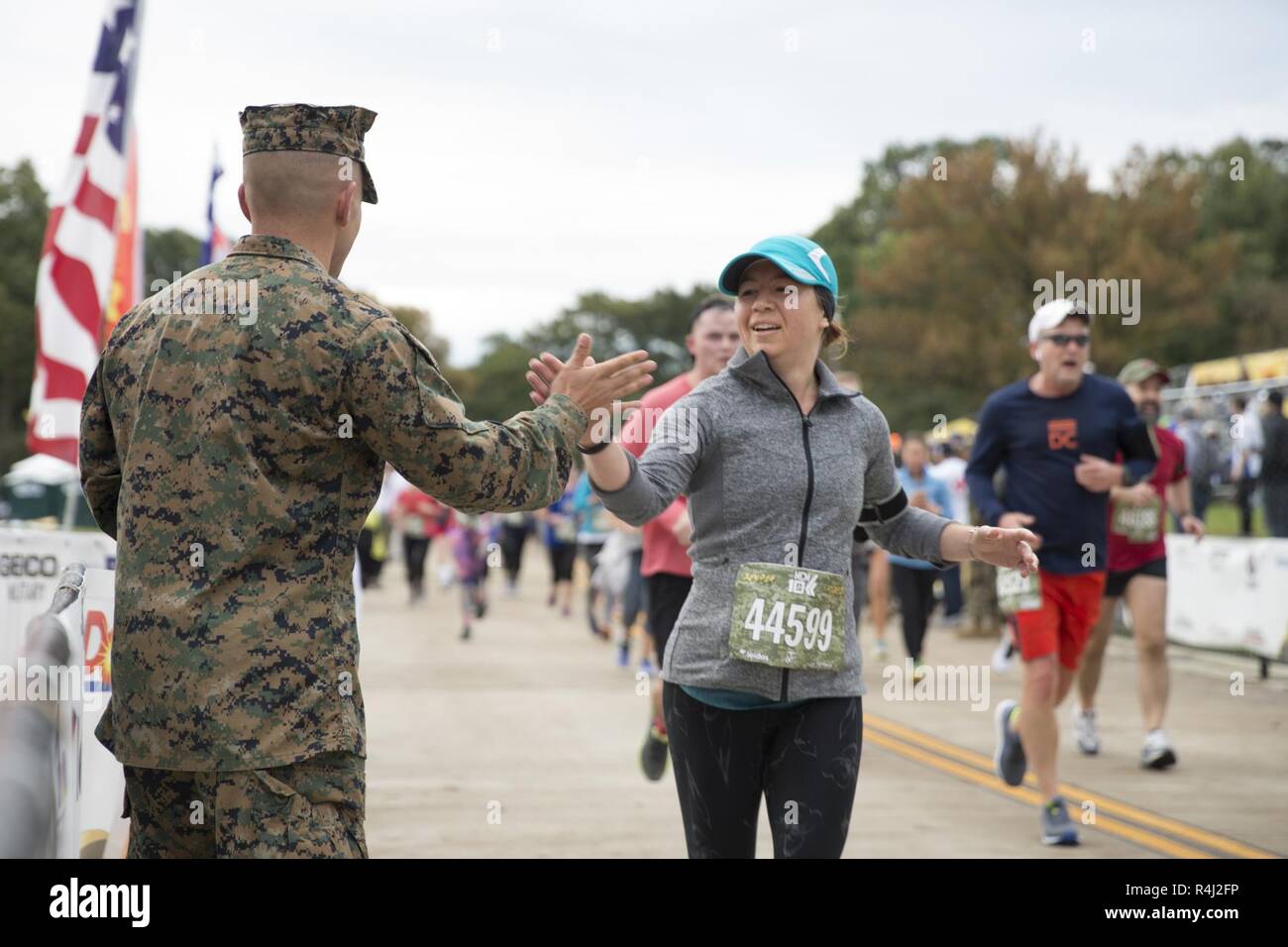 A participant of the 43rd Marine Corps Marathon 10K high fives a Marine as a she runs towards the finish line at the Marine Corps War Memorial, Arlington, Va., Oct. 28, 2018. Also known as 'The People's Marathon,' the race drew roughly 30,000 participants to promote physical fitness, generate goodwill in the community, and showcase the organizational skills of the Marine Corps. Stock Photo