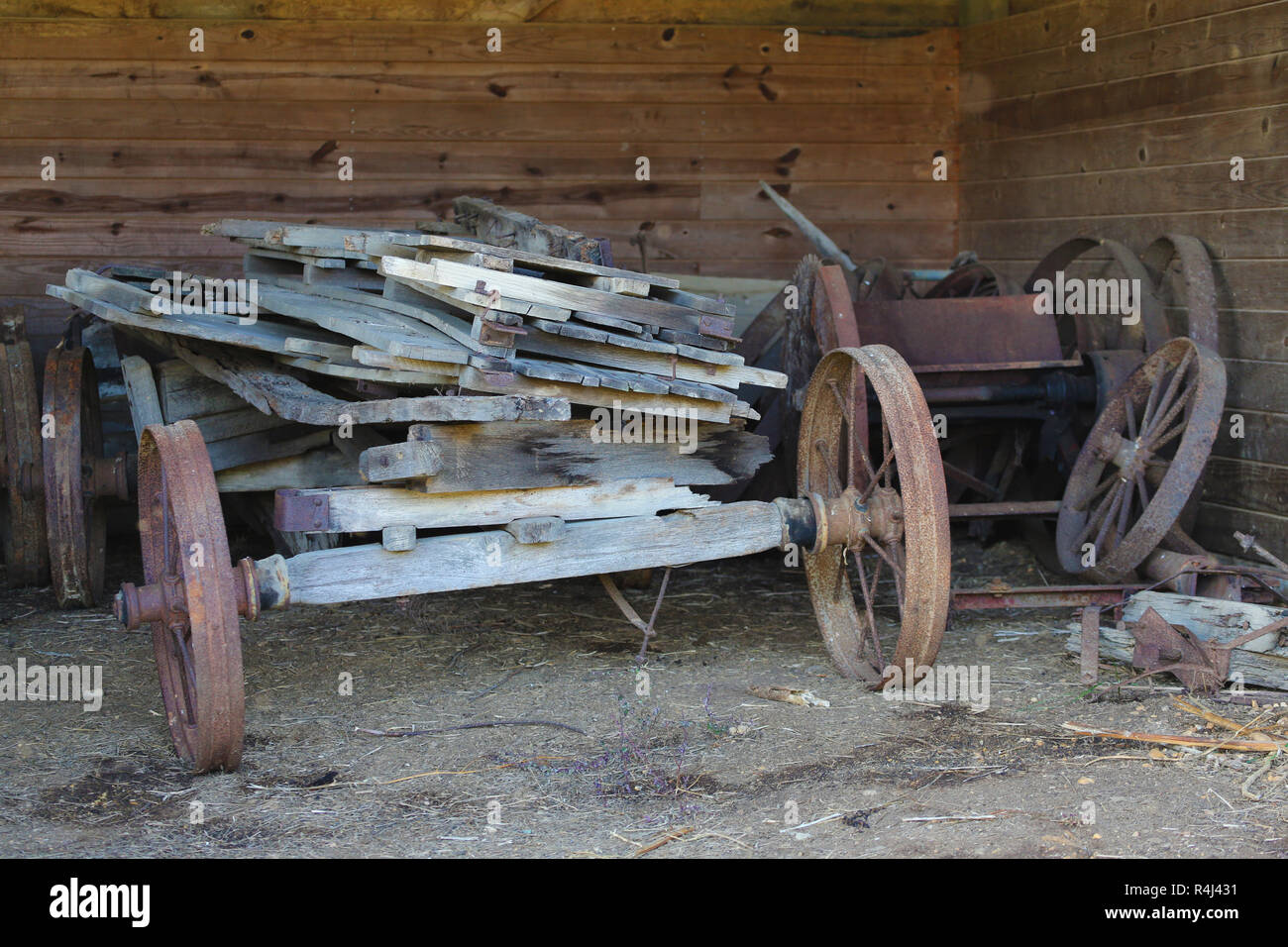 old rickety farm wagon loaded with lumber and wheels leaning against shed wall Stock Photo