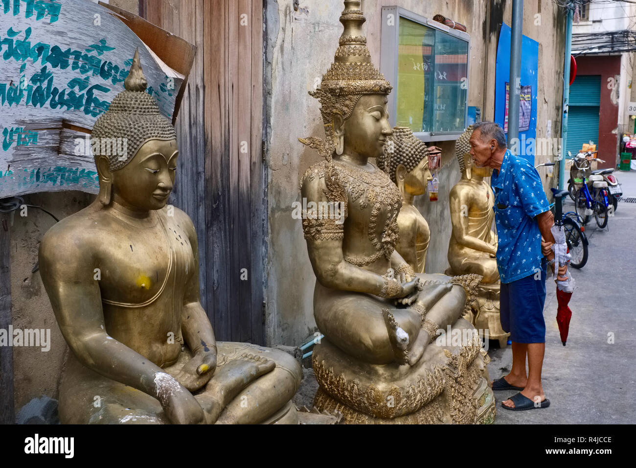 Outside a factory for Buddha statues in Bamrung Muang Road in Bangkok, Thailand, a man looks inensely at a statue placed outside for delivery Stock Photo