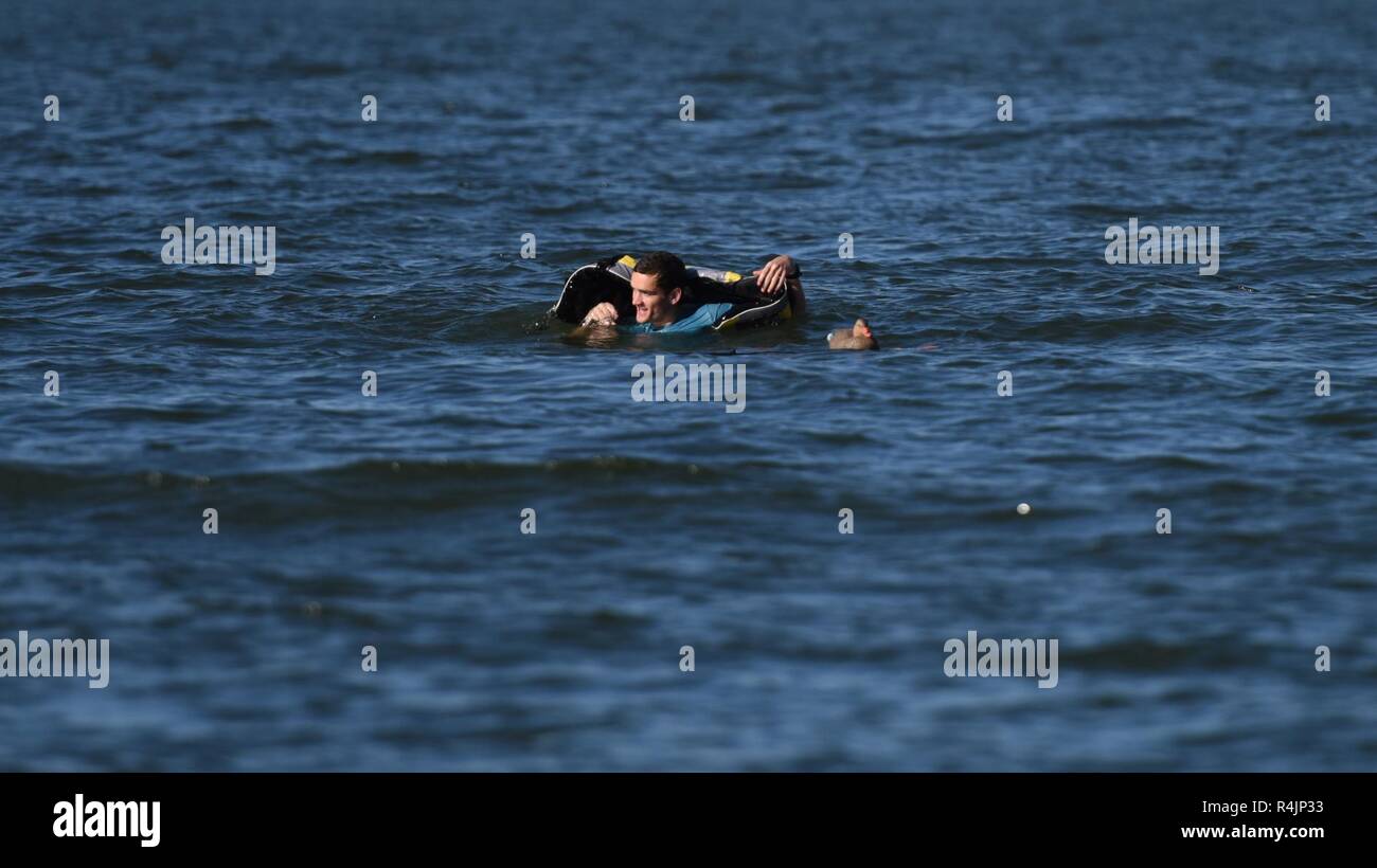 Coast Guard Seaman Benjamin Woodward, a crew member at Station Cape Charles, Virginia, attempts to don a life jacket during a demonstration in the Chesapeake Bay, Oct. 30, 2018. The station’s crew explained the dangers of cold water to local media members and emphasized the importance of wearing life jackets underway. Stock Photo