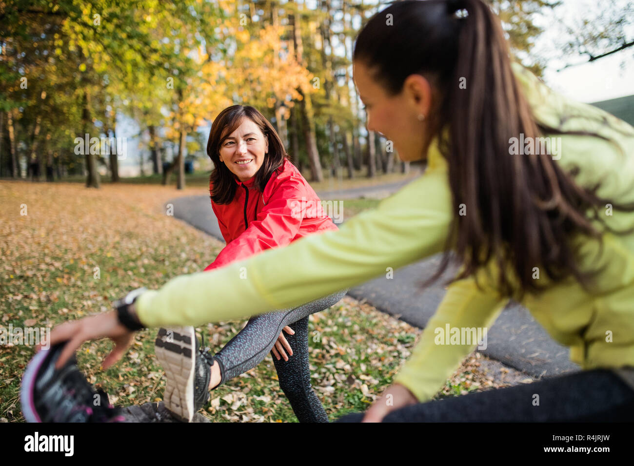 Two female runners stretching legs outdoors in park in autumn nature. Stock Photo