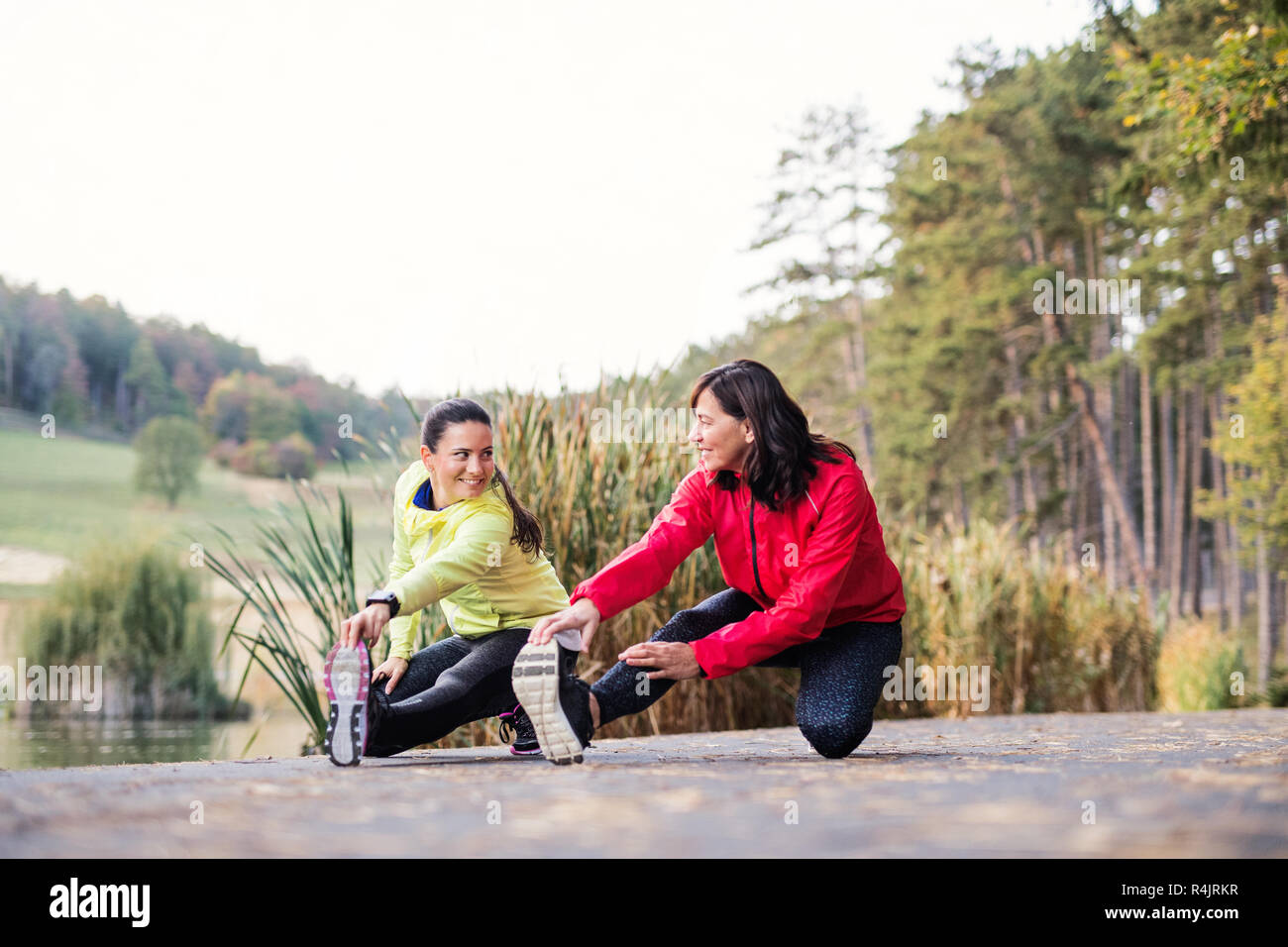 Two female runners stretching legs outdoors in park in autumn nature. Stock Photo