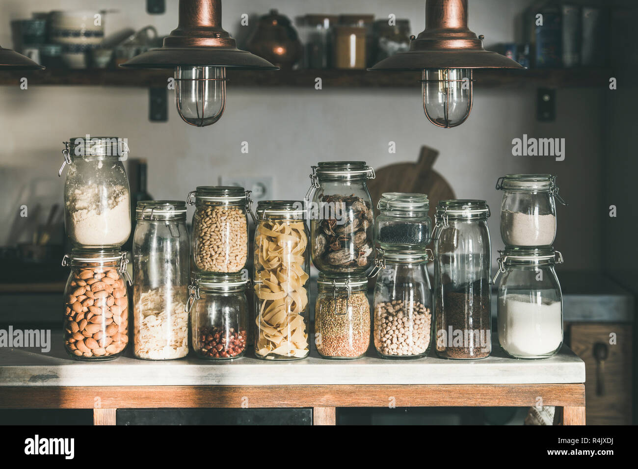 Rustic kitchen food storage arrangement. Grains, cereals, nut, dry fruit, flour, pasta kinds in jars over concrete kitchen counter. Clean eating, heal Stock Photo