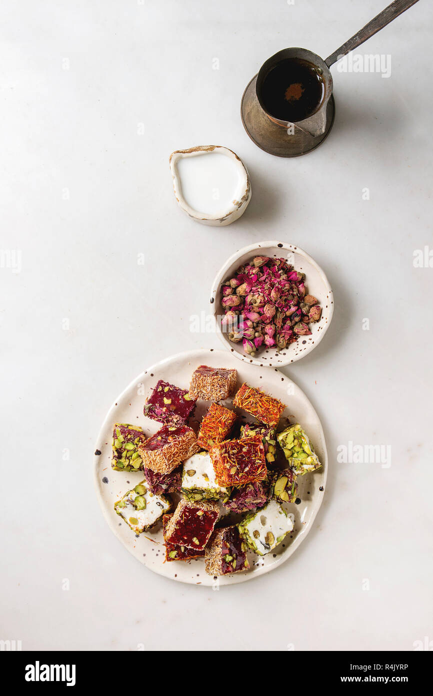 Variety of traditional turkish dessert Turkish Delight with rose petals and pistachio nuts on ceramic plate with coffee jezve and milk jug over grey s Stock Photo