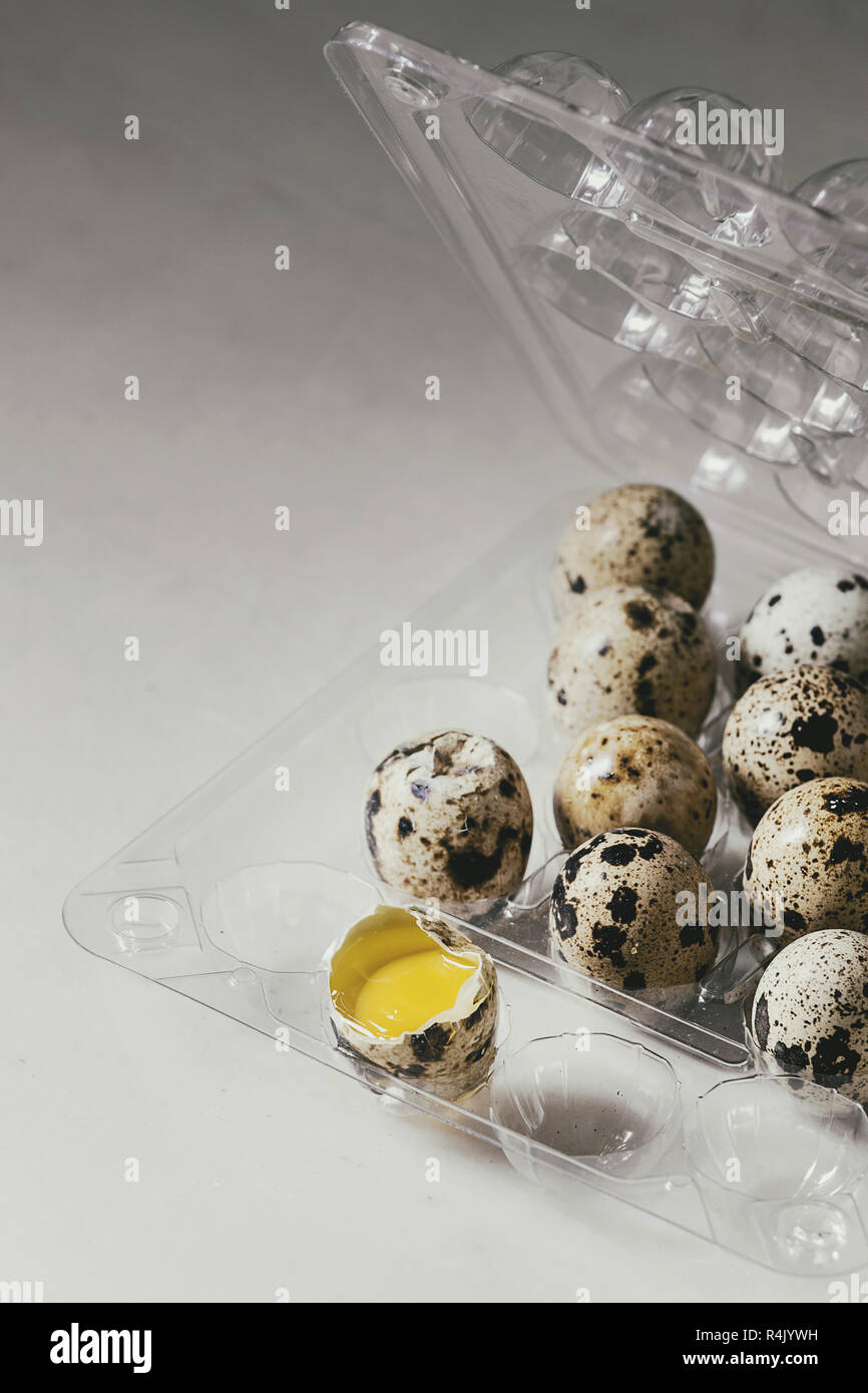 Raw uncooked quail eggs whole and broken in plastic boxing on white