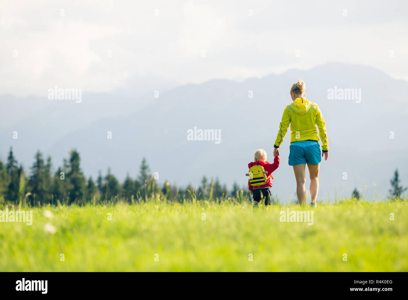 Happy mother with baby boy walking on green meadow. Hiking adventure with child on summer family trip in mountains. Vacations or weekend activity with Stock Photo