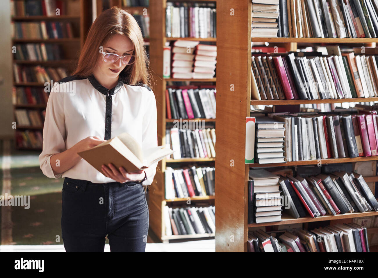 Young Attractive Student Librarian Reading A Book Between Library ...