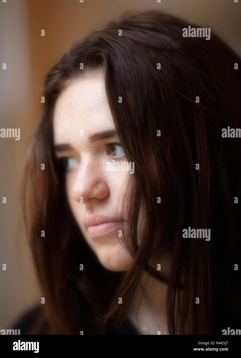 Image of young girl looking thoughtful, face lit by window light at f1.2 so blurred background, bokeh Stock Photo