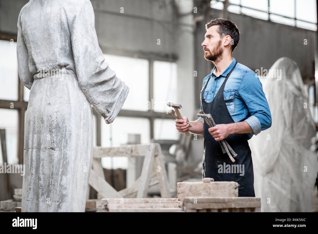 Handsome sculptor standing with working tools near the sculpture in the