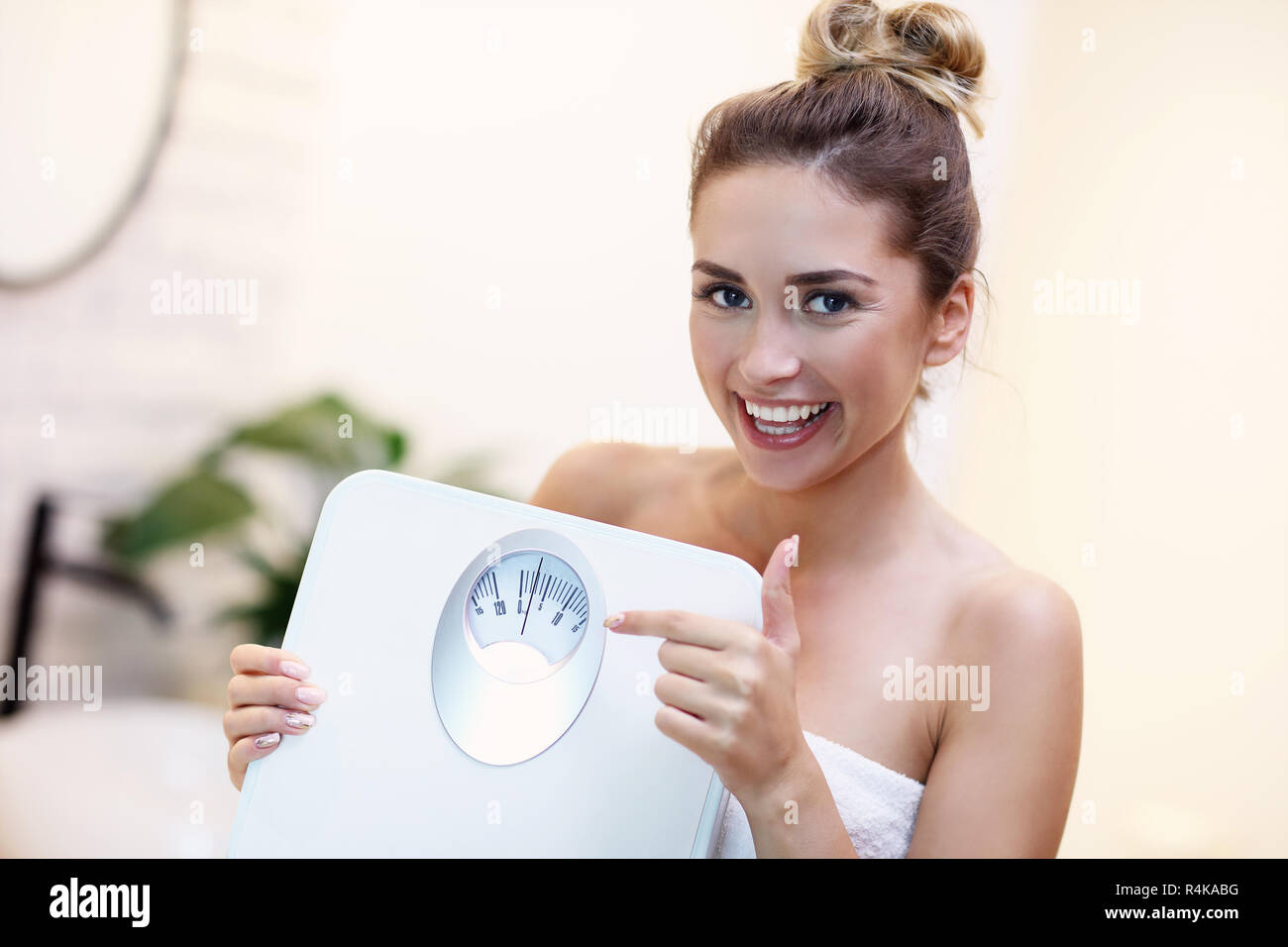 Happy woman holding bathroom scales in bathroom Stock Photo