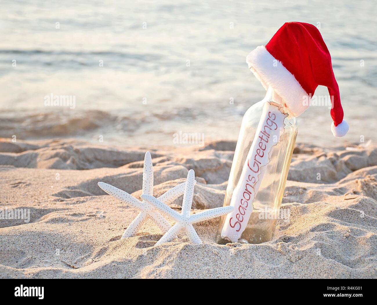 Santa hat on message in a bottle with white starfish in beach sand and Season's Greetings sign Stock Photo