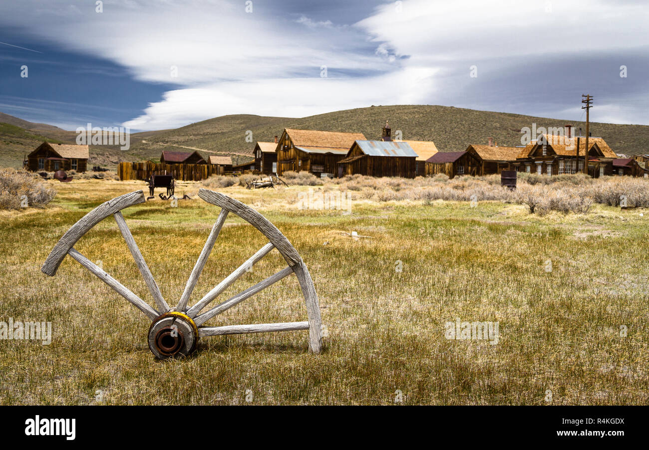 Remains of old cart wheel with abandoned ghost town Bodie in the background, California Stock Photo