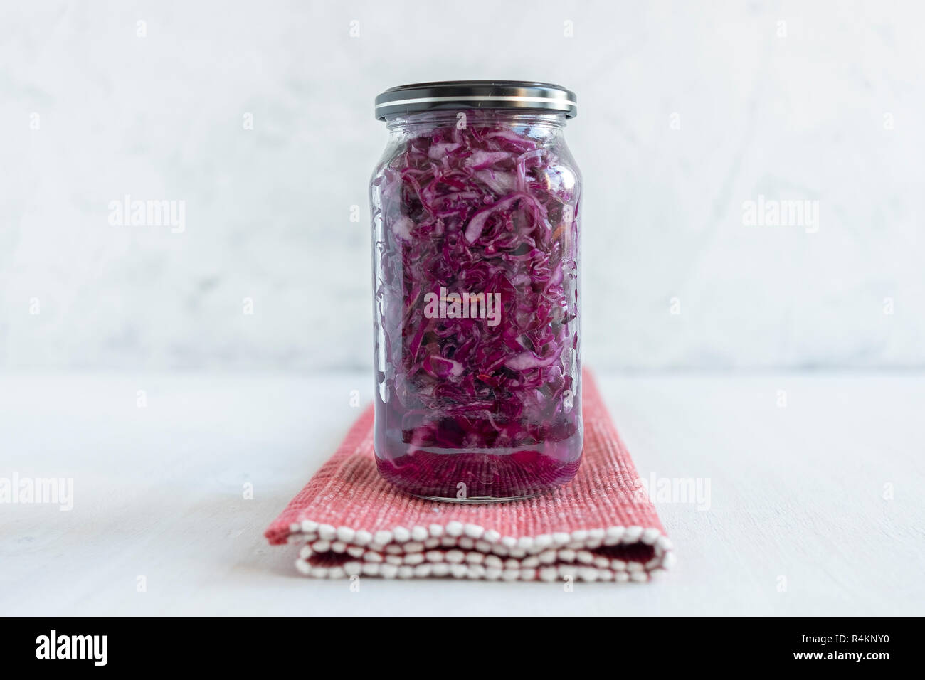 Sealed glass jar with yummy purple sauerkraut standing on napkin on white background Stock Photo