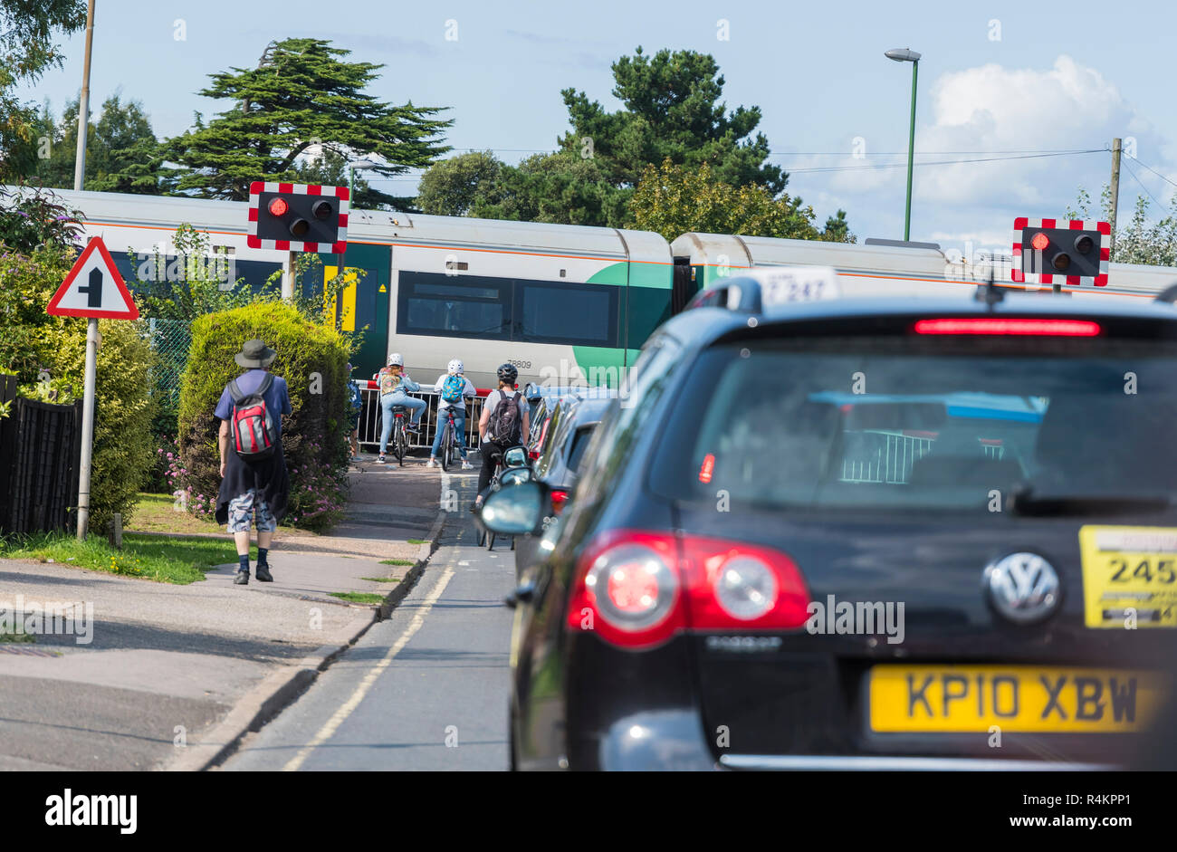 Cars and people waiting and queuing at a level crossing with a Southern Rail train going past in West Sussex, England, UK. Stock Photo