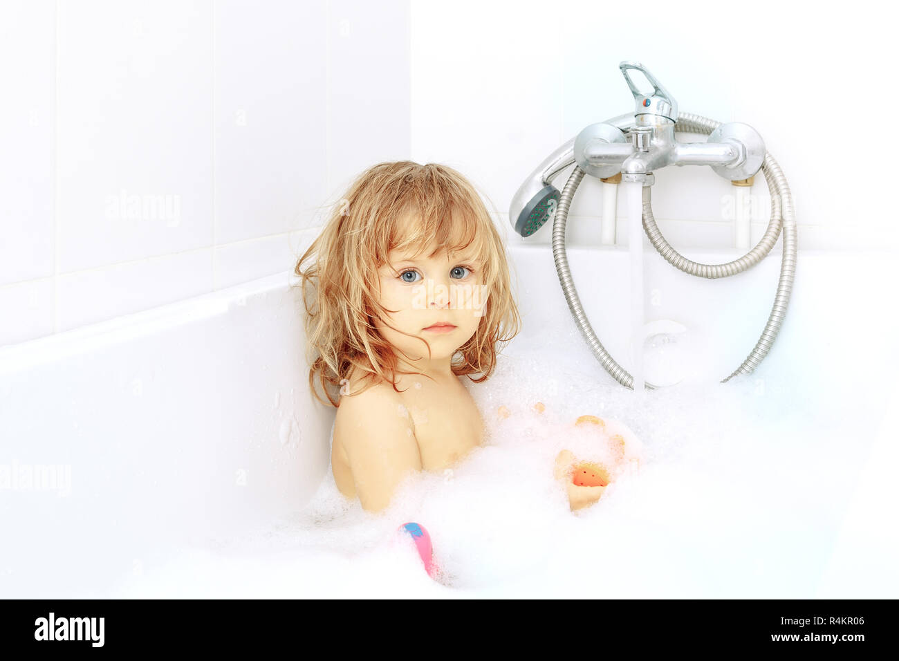 Active cute little blond toddler girl of 2 years having fun with water by taking bath in bathtub at home. Funny kid splashing and playing with toys. S Stock Photo