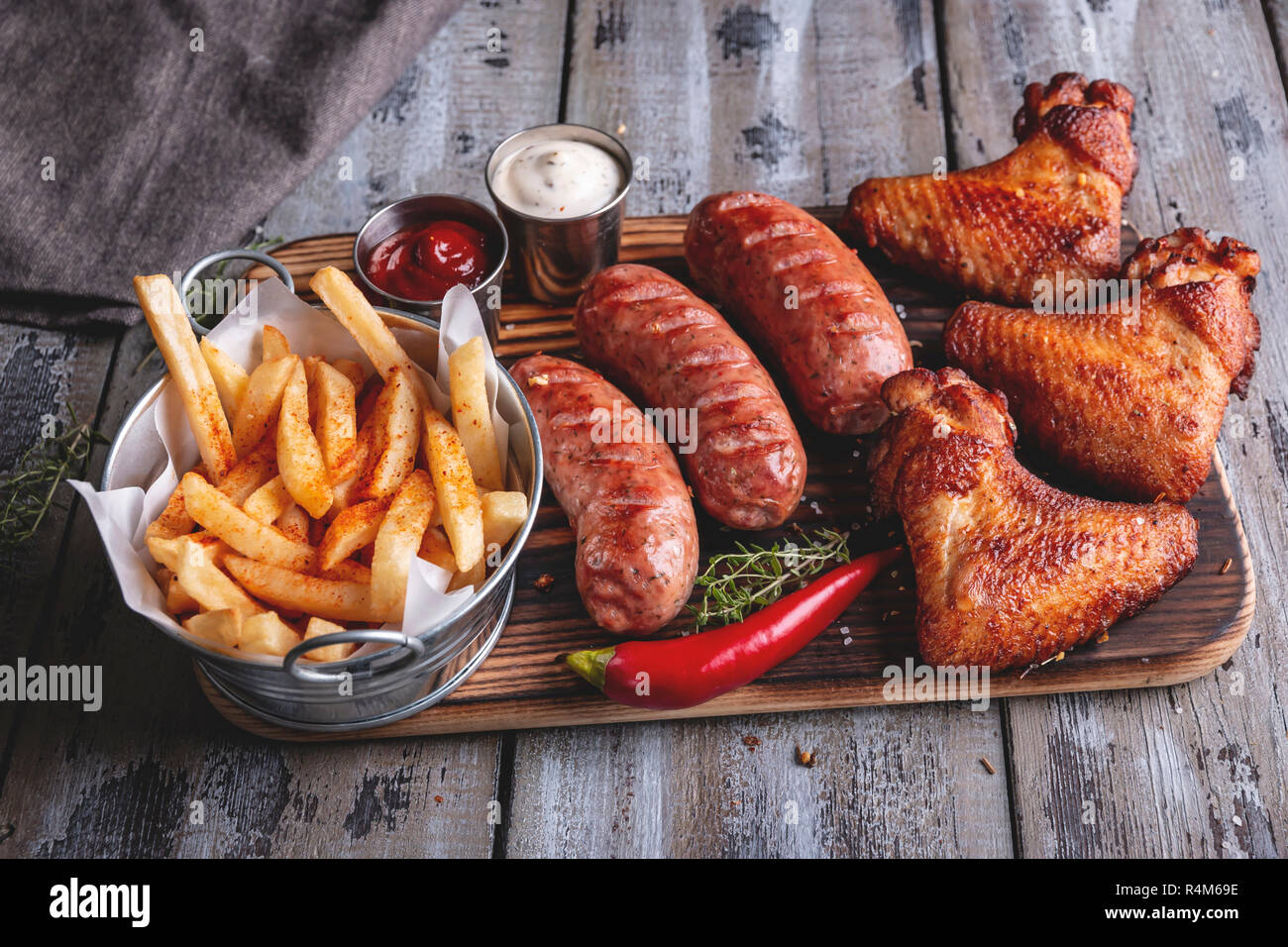 Grilled chicken wings,sausages, french fries, white and red sauce on a wooden surface Stock Photo