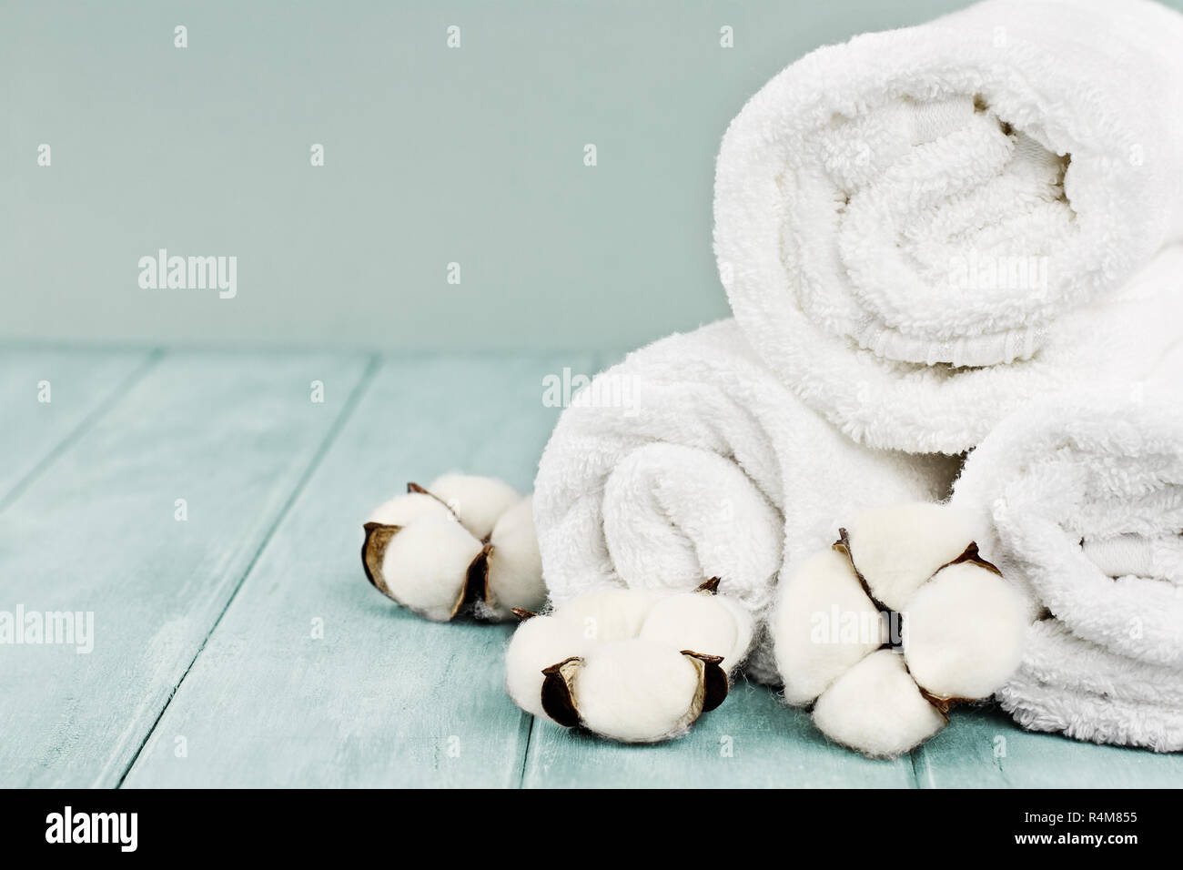 Rolled up white fluffy towels with cotton flowers against a blurred blue background with free space for text. Stock Photo