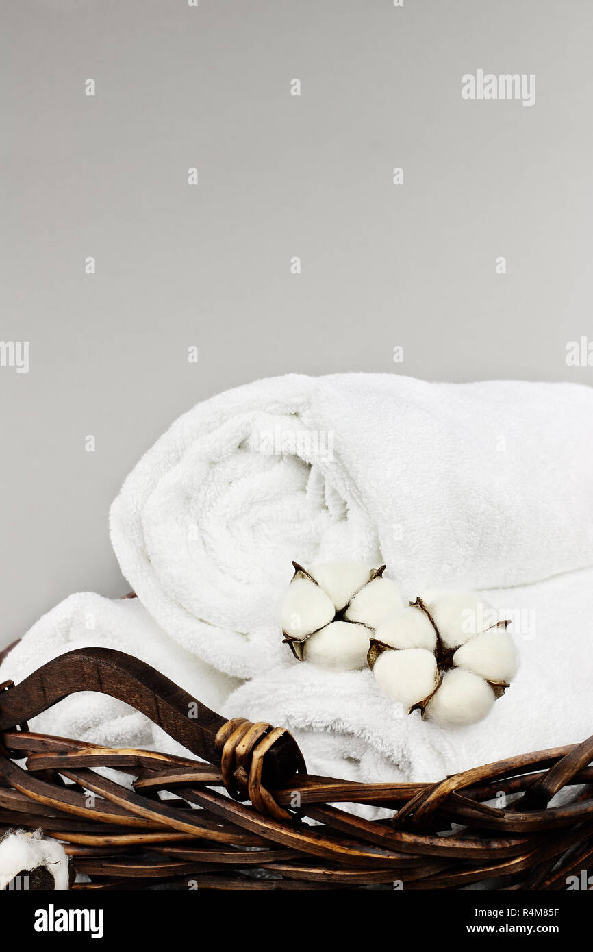 Laundry basket filled white fluffy towels, cotton flowers and a bottle of liquid soap against a grey background with free space for text. Stock Photo