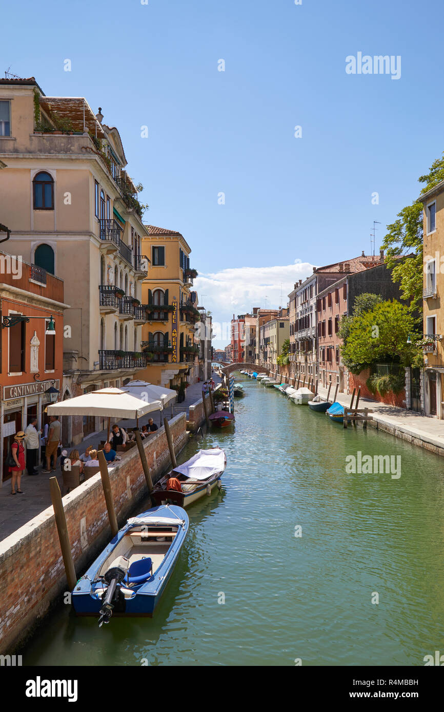 VENICE, ITALY - AUGUST 14, 2017: Canal with Italian restaurant and sidewalk tables with people in Venice in a sunny summer day Stock Photo