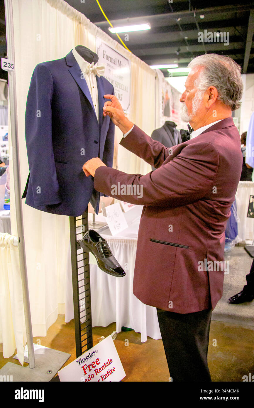 Formally-dressed himself, a formal wear supplier spiffs up a blue tuxedo on exhibit along with a black shoe at a bridal festival in Costa Mesa, CA. Stock Photo