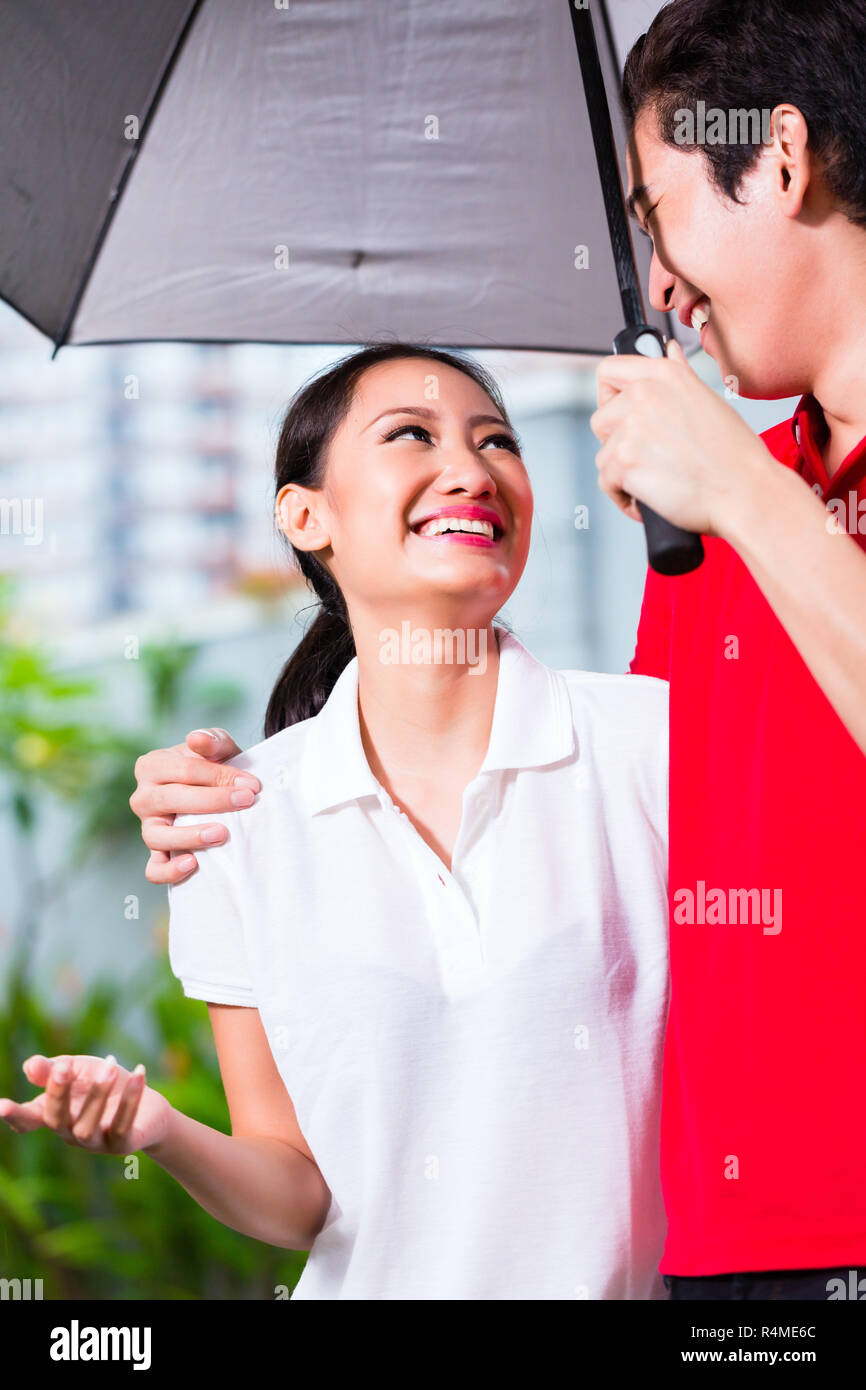 Asian couple walking with umbrella through rain Stock Photo - Alamy