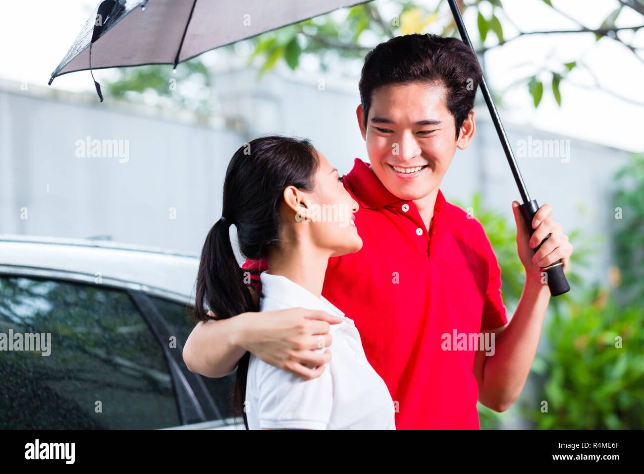 Asian couple walking with umbrella through rain Stock Photo - Alamy
