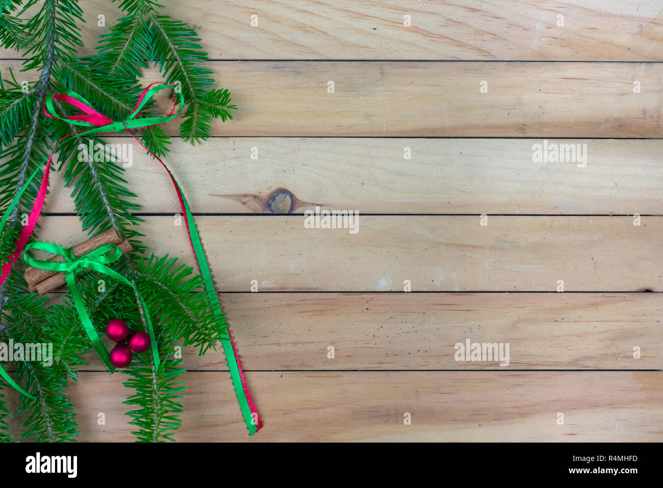 A spruce bough with a red and green ribbon bow, cinnamon sticks, and red berries  on a wooden slat background with copy space Stock Photo