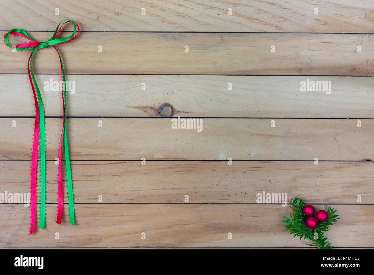 A red and green ribbon bow along the left side with a red berry cluster on balsam fir on bottom right corner on wooden slat background with copy space Stock Photo