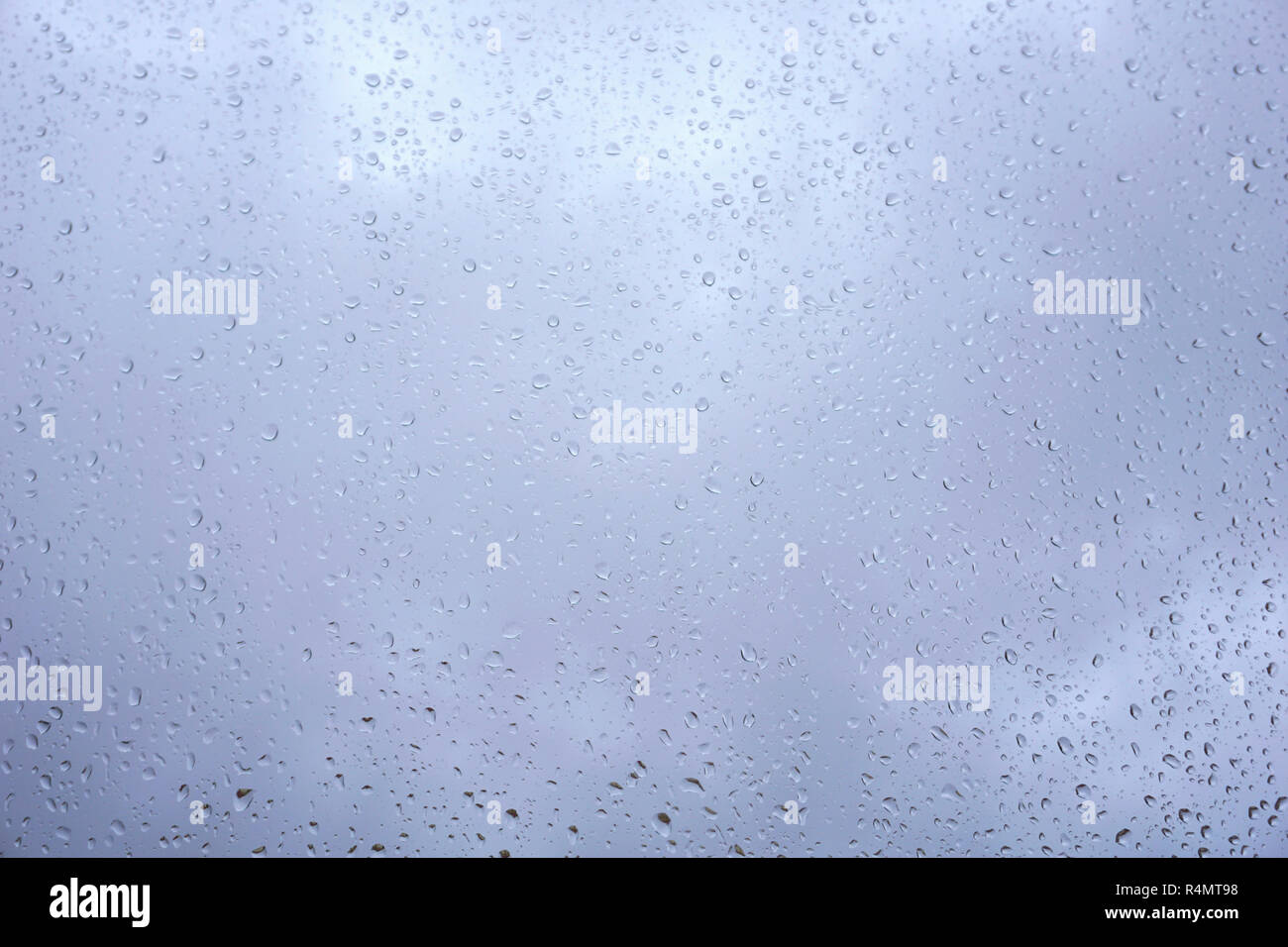 Cloudy blue sky behind window glass full of rain drop. Water drops pattern background Stock Photo