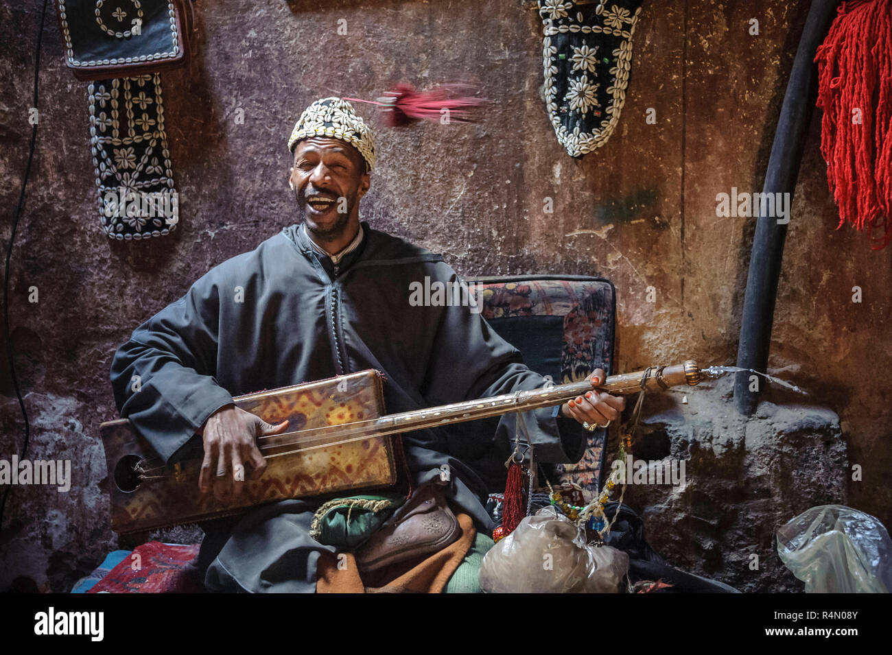 18-04-11. Marrakech, Morocco. A musician sitting cross legged and playing a traditional three stringed guembri musical instrument. He wears a fez hat Stock Photo
