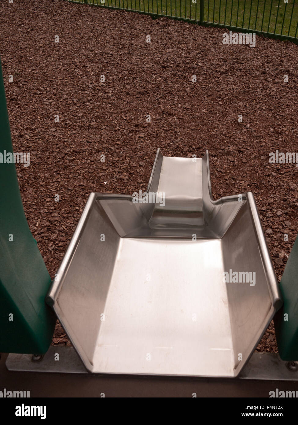 a close up shot of a metal slide in a child's playground with bark wooden chips for safety, accident, no people shining metal, dangerous and fun for children and parents Stock Photo