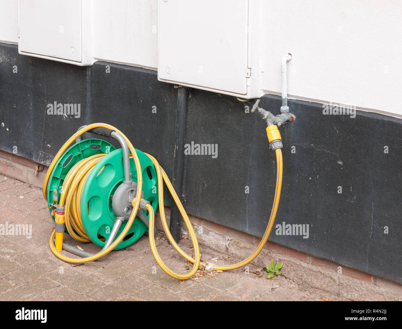 a rolled up hose plugged into the tap at the side of a house with no
