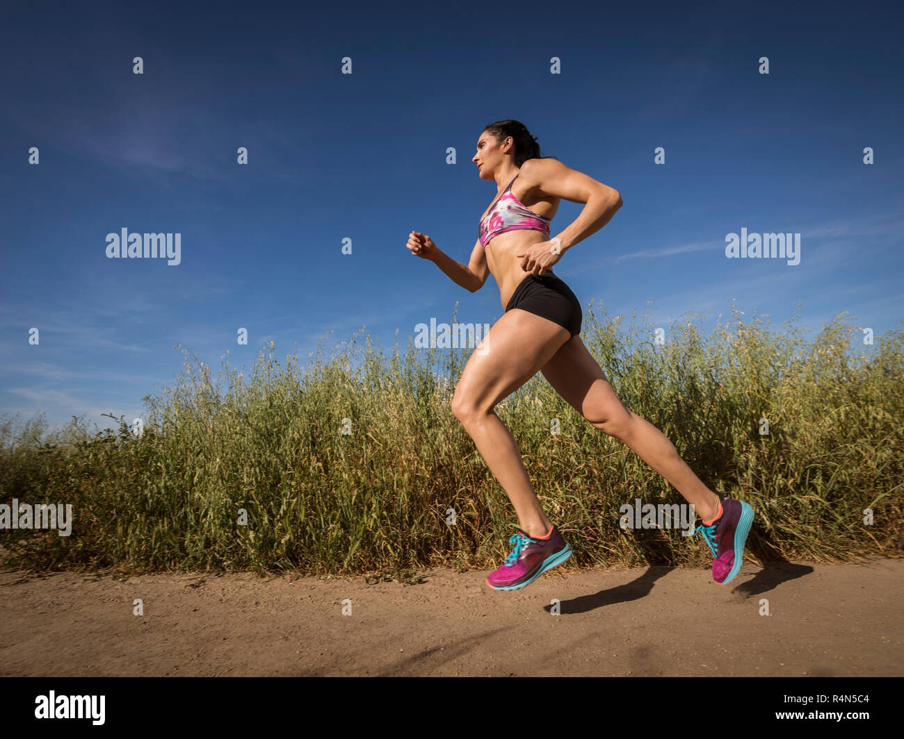 Mid adult woman jogging on path through field Stock Photo