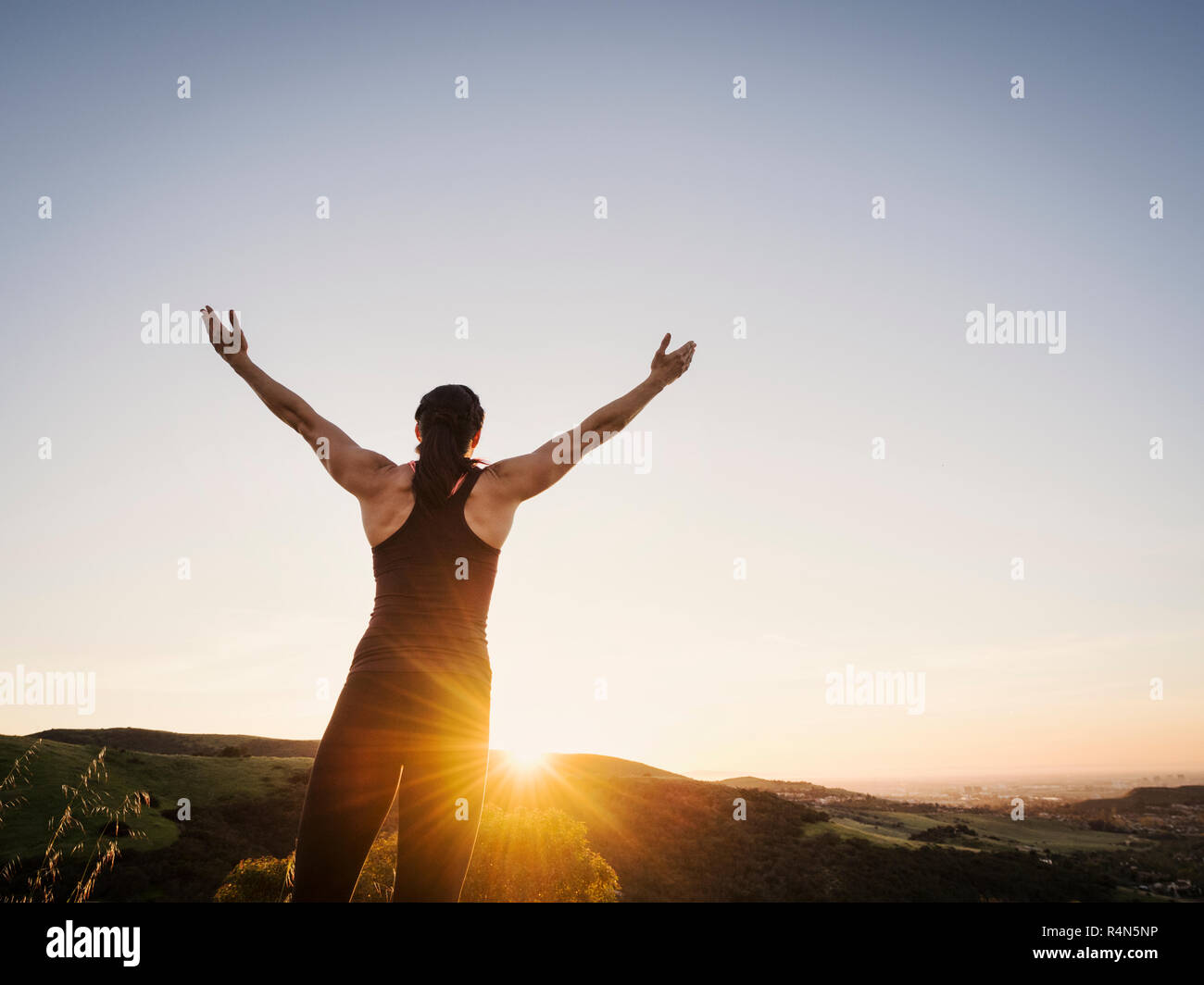 Rear view of woman with arms raised at sunset Stock Photo