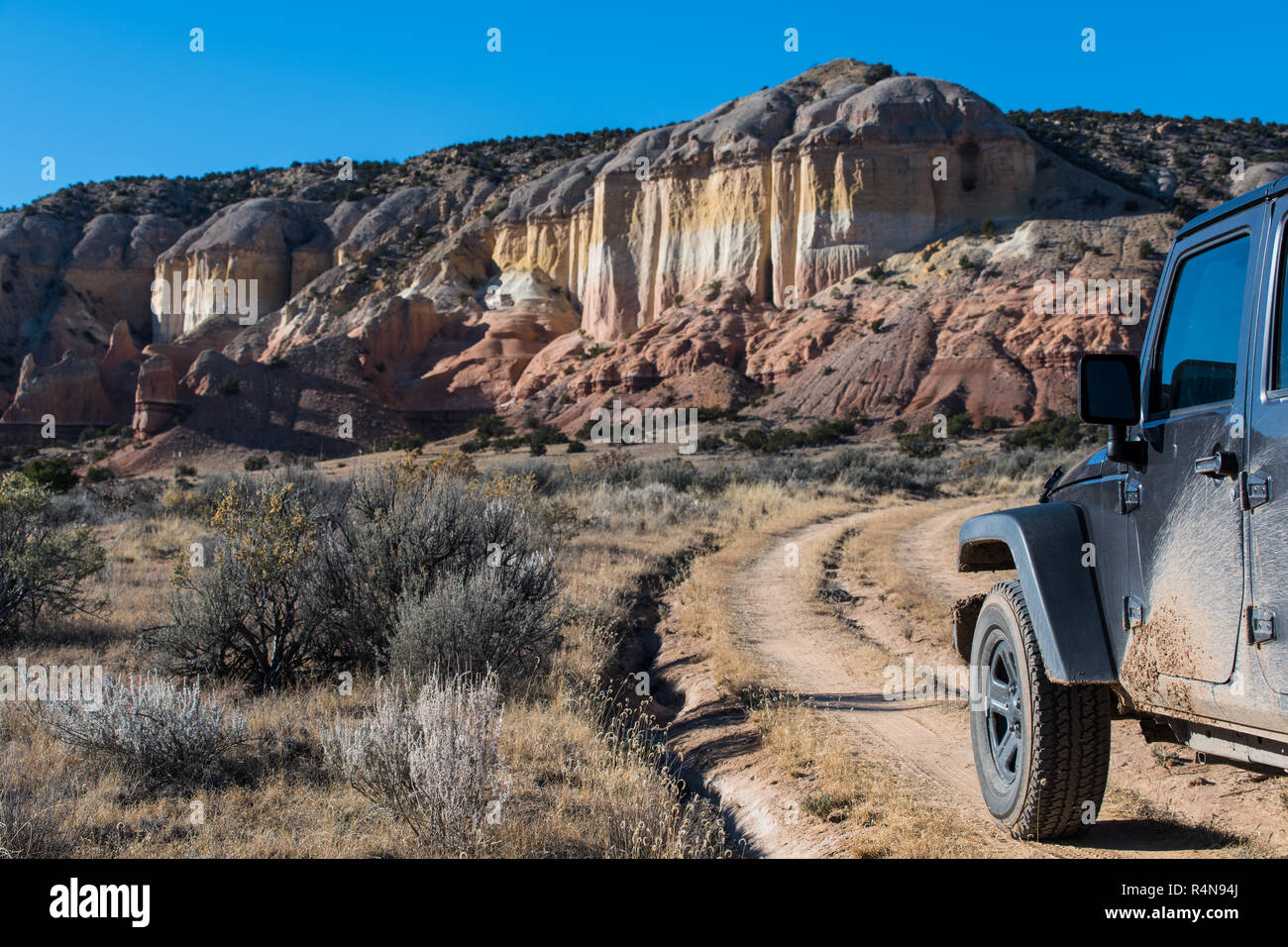 Muddy four-wheel drive vehicle on dirt road heading toward a colorful mesa in the desert landscape in the Rio Chama canyon near Santa Fe, New Mexico Stock Photo