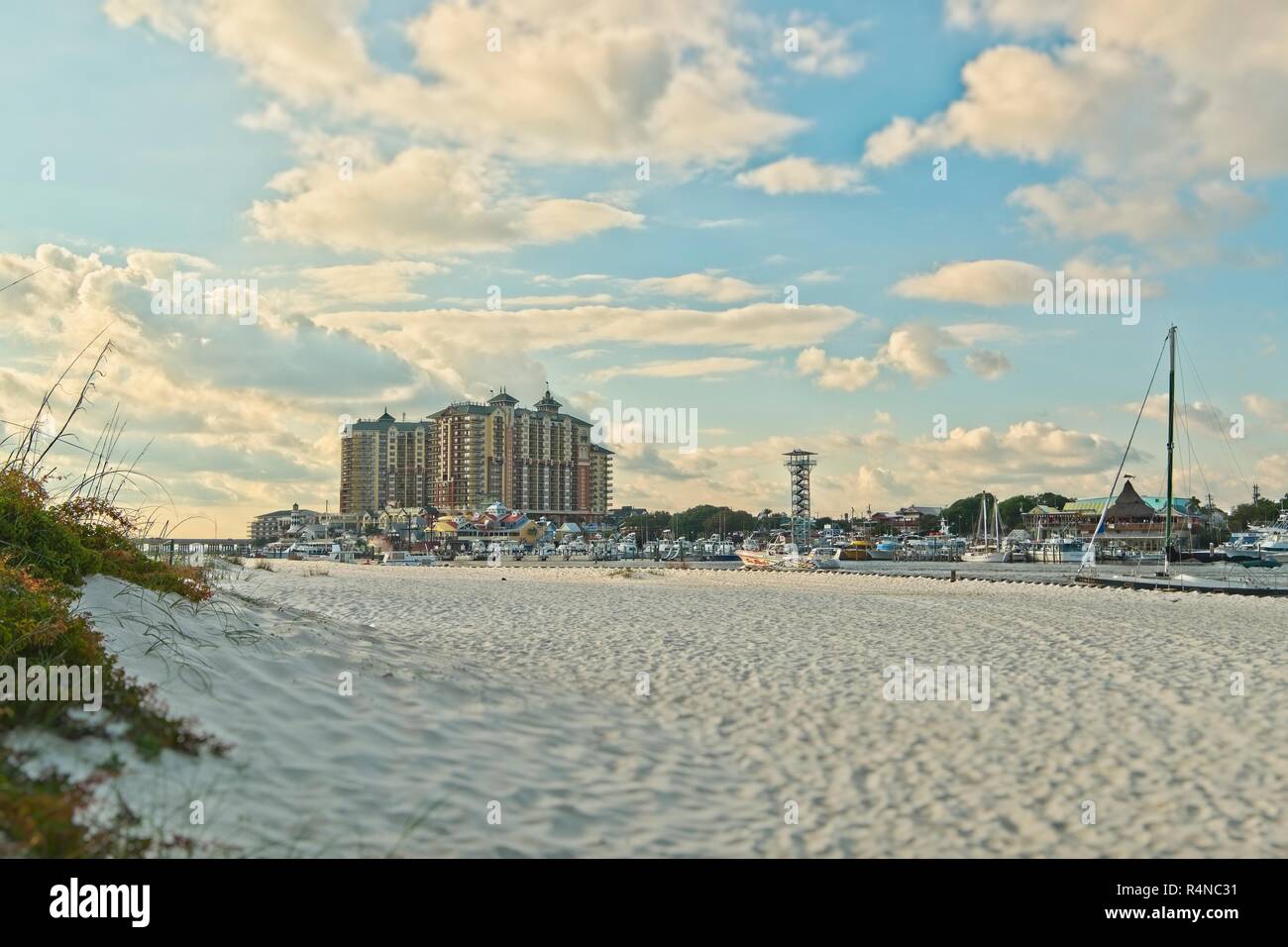 White sand beach and dune with the Emerald Grande at HarborWalk Village and the Destin Florida commercial sport fishing fleet tied up at the marina. Stock Photo