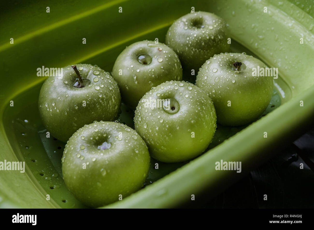Green apples in a washing basket with water droplets on their skin. Stock Photo