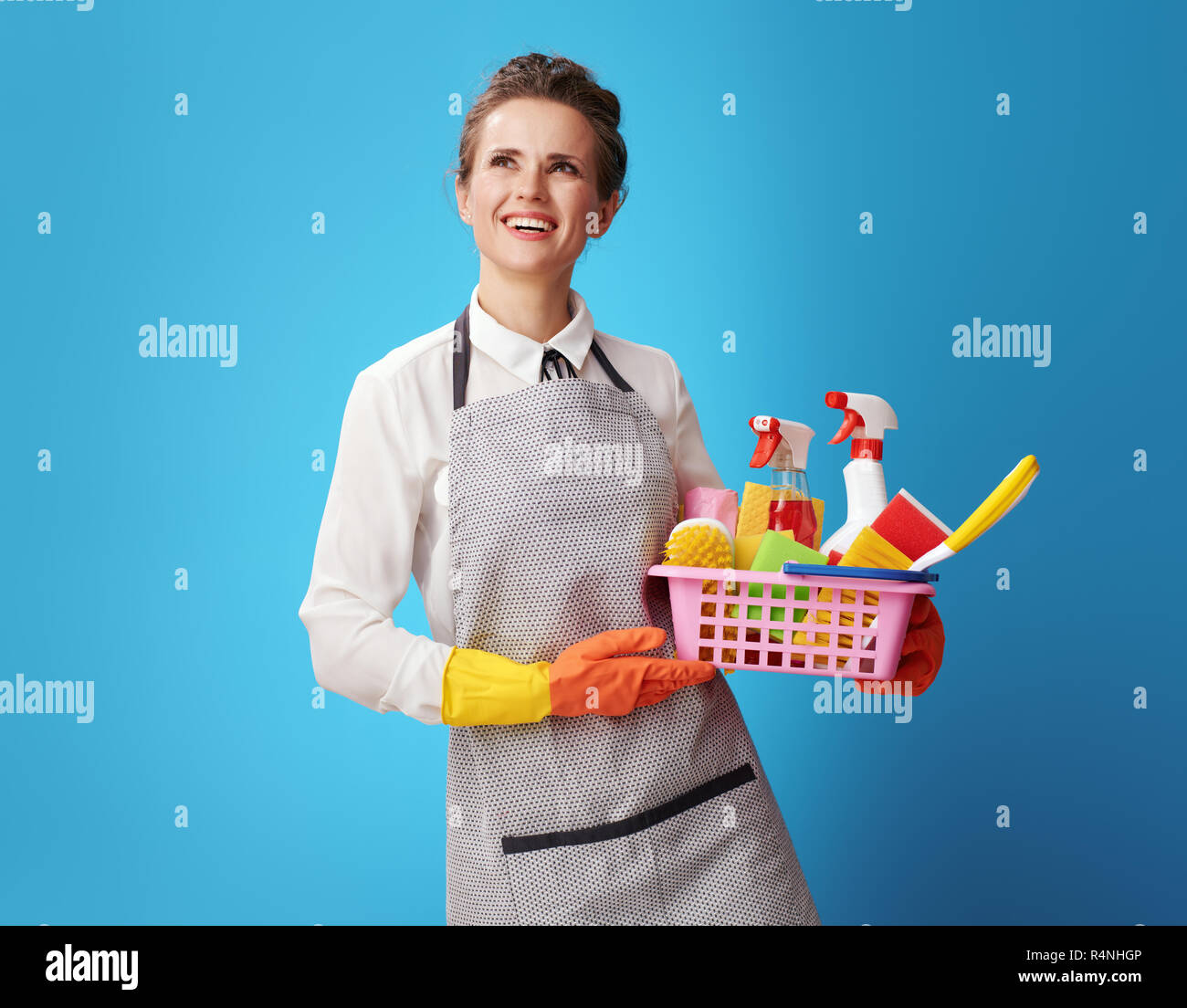 Portrait of smiling young cleaning woman in apron with a basket with ...