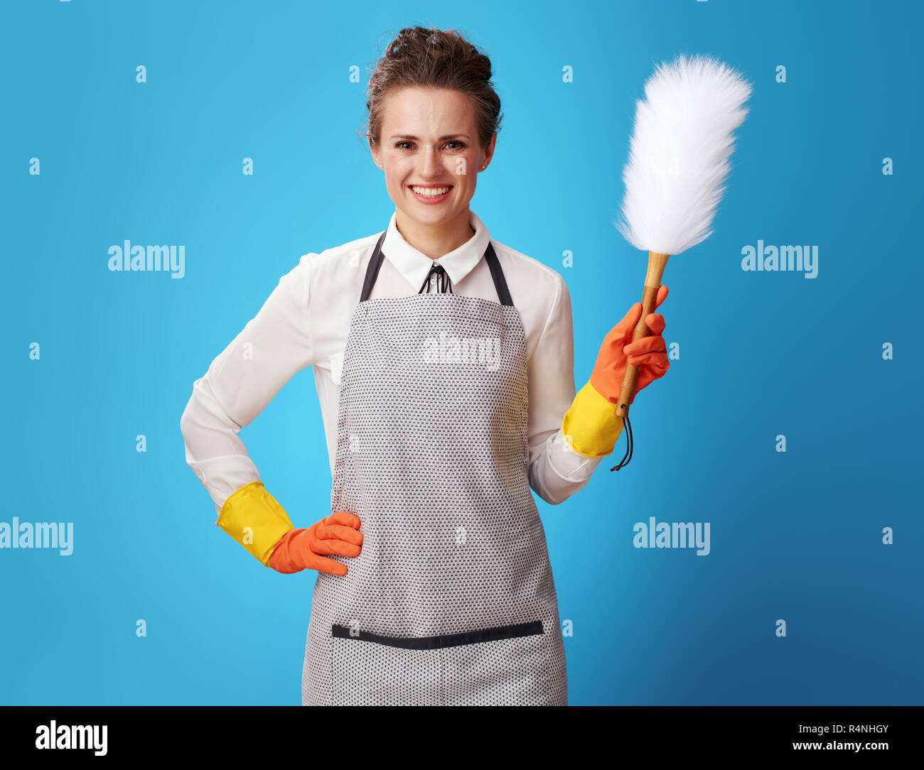 happy young housemaid in apron with dust cleaning brush isolated on blue. How cleaning business working? Simply - we perfectly clean what you want and Stock Photo