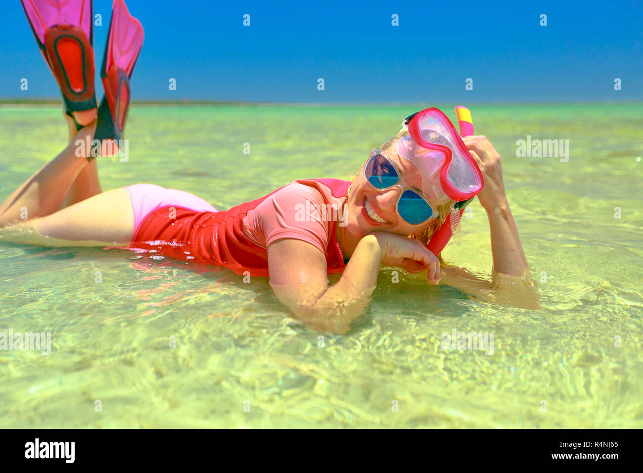 happy lifestyle woman with snorkeling wetsuit, mask and fins pink and peach color, sunbathing lying in a natural pool of Little Lagoon in Shark Bay, Denham, Western Australia. Stock Photo