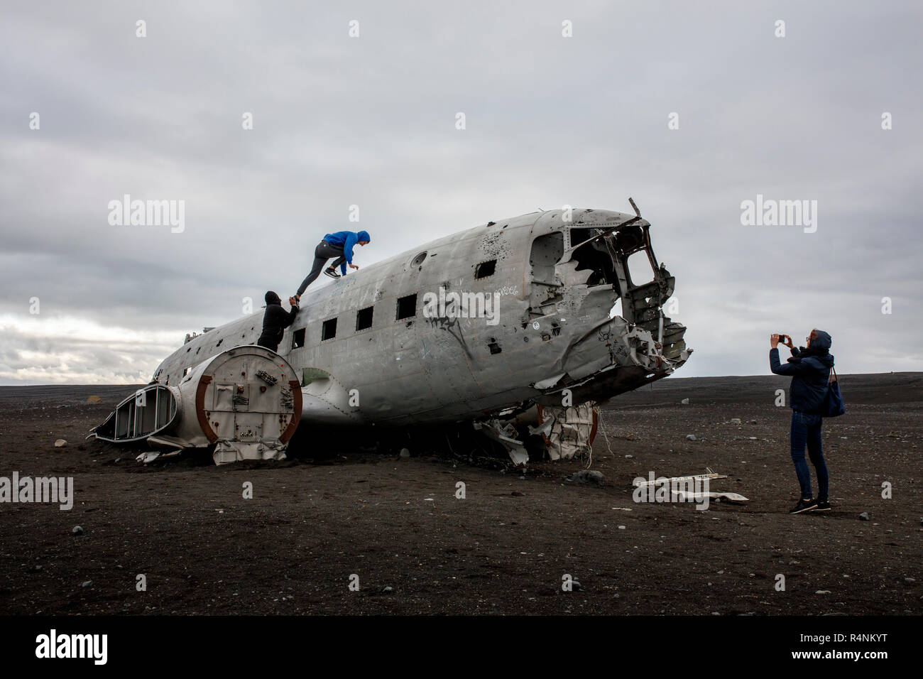 Tourists climb on top of the wreckage of a US Navy DC plane that crash landed on a beach in Southern Iceland on November 21, 1973. The place crashed as a result of either low fuel or icing on the engines and all aboard survived. After the crash the Navy stripped the plane of engines and other valuable components but left the main fuselage on the black sand beach near Solheimasandur. Today, due in large part to geotagging from Instagram, the plane is a popular destination for photographers and adventure enthusiasts visiting Iceland. Stock Photo