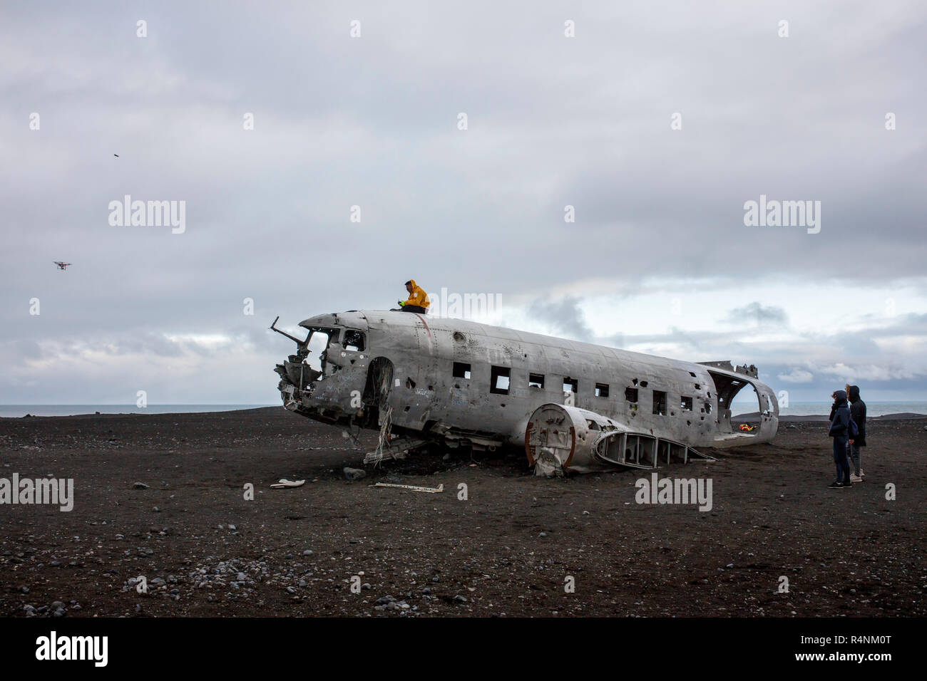 A tourist takes selfies with a drone as he sits on top of the wreckage of a US Navy DC plane that crash landed on a beach in Southern Iceland on November 21, 1973. The place crashed as a result of either low fuel or icing on the engines and all aboard survived. After the crash the Navy stripped the plane of engines and other valuable components but left the main fuselage on the black sand beach near Solheimasandur. Today, due in large part to geotagging from Instagram, the plane is a popular destination for photographers and adventure enthusiasts visiting Iceland. Stock Photo