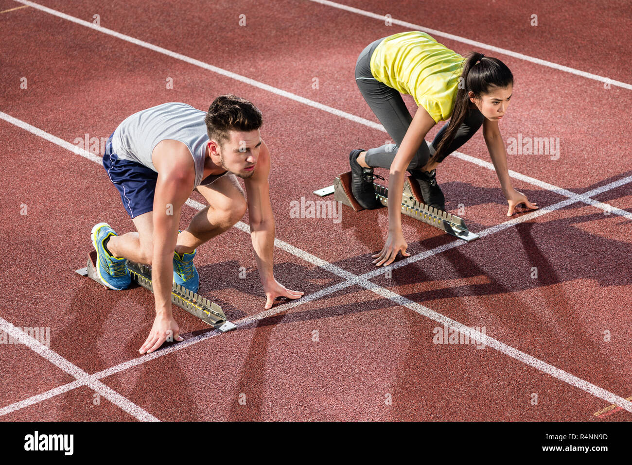 Male and female athlete in starting position at starting block of