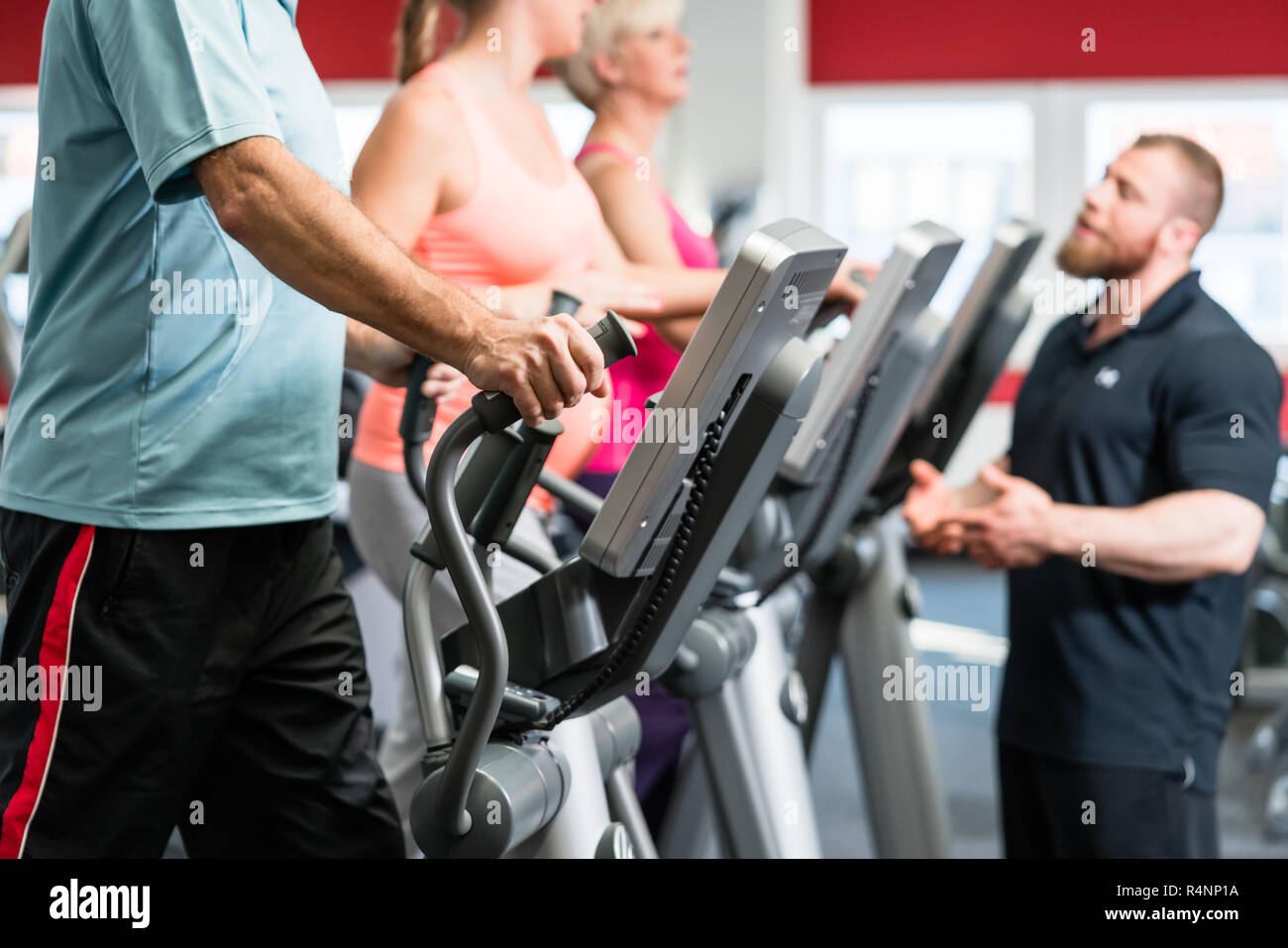 Seniors training on cross trainer with personal trainer at the gym